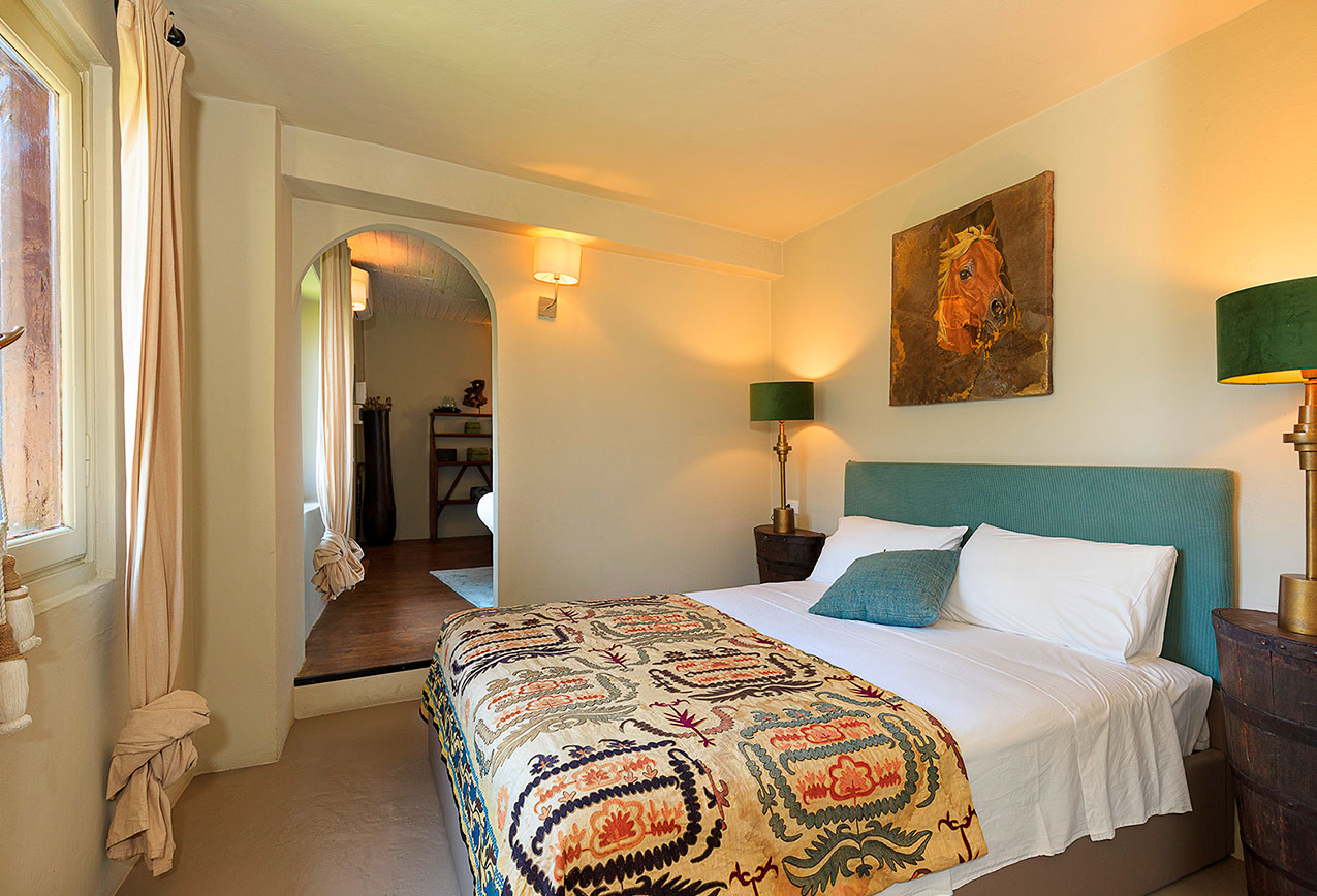 villa-wirnica-la-canonica-suite-cozy-bedroom-archway-entrance Cozy bedroom in La Canonica Suite showing colorful patterned bedding and archway entrance to the living area.